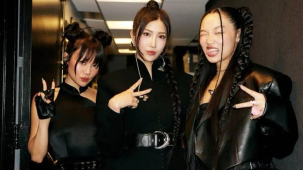 Musicians Ejae, Audrey Nuna, and Rei Ami pose together backstage at the Oscars 2026. They are dressed in sleek, coordinated black outfits with edgy styling, including leather accents and unique braided hairstyles, while making peace signs for the camera.