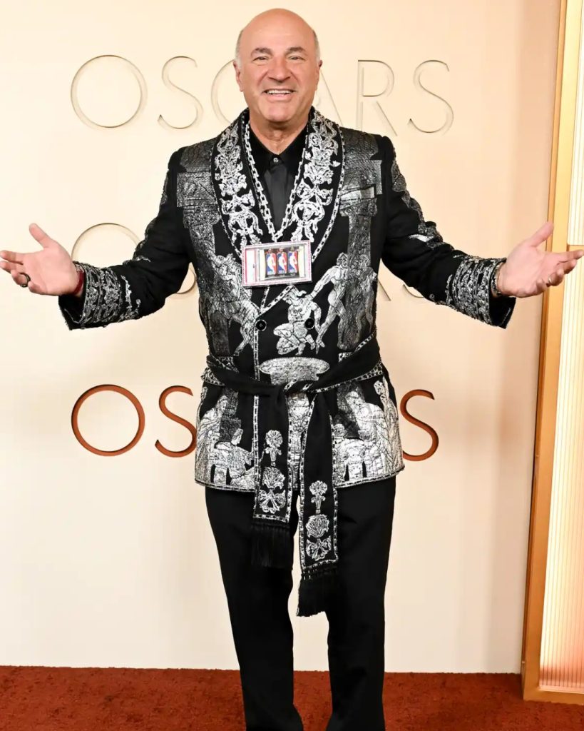Kevin O'Leary in a classic black tuxedo paired with his signature red pocket square and a high-end luxury watch.