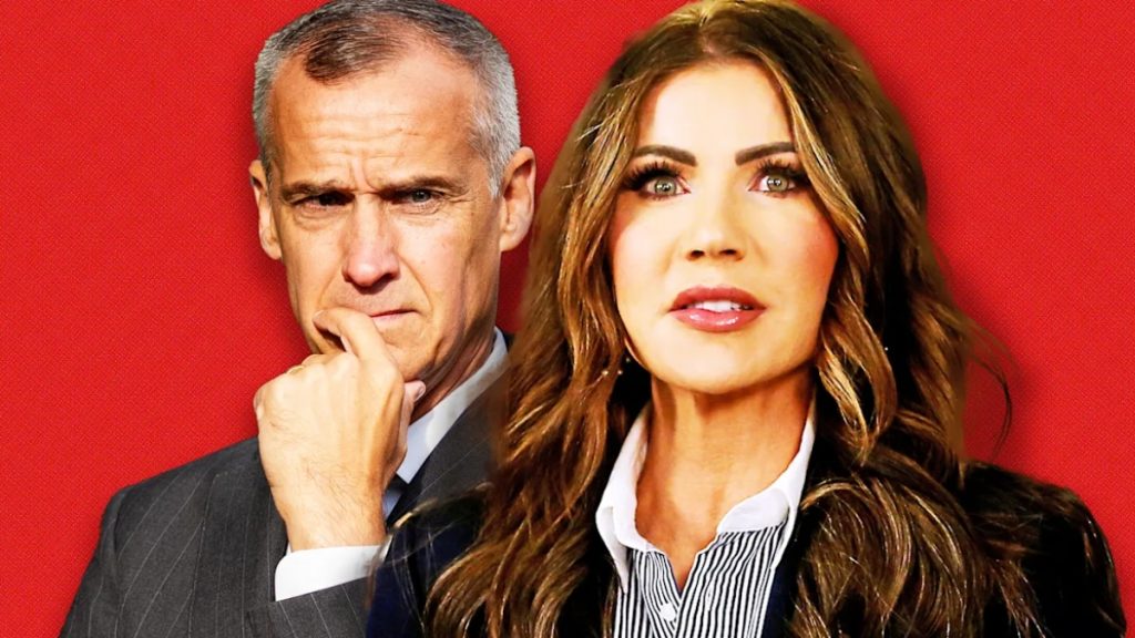 A composite image featuring Kristi Noem in the foreground and Corey Lewandowski in the background, highlighting the Kristi Noem Corey Lewandowski scandal. Noem is wearing a dark navy blazer over a striped shirt, while Lewandowski, in a grey suit, has his hand to his chin in a pensive gesture against a solid red backdrop