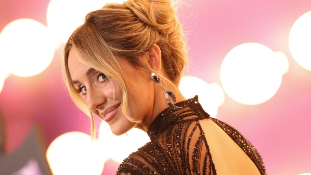 A close-up shot of a smiling Lainey Wilson in an elegant black dress with a chic updo, captured during the lively Hannah Montana reunion.