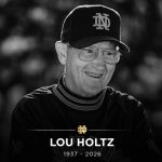 A black-and-white memorial tribute image of Lou Holtz wearing a Notre Dame cap and pullover. The bottom of the image features a gold Notre Dame "ND" logo above the text "LOU HOLTZ 1937 - 2026