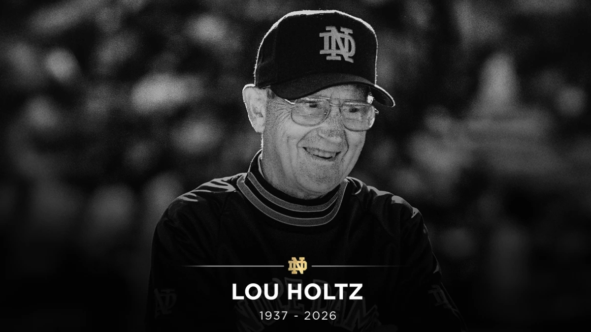 A black-and-white memorial tribute image of Lou Holtz wearing a Notre Dame cap and pullover. The bottom of the image features a gold Notre Dame "ND" logo above the text "LOU HOLTZ 1937 - 2026