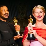 A celebratory side-by-side shot of Michael B. Jordan and Jessie Buckley holding their Academy Awards. Michael B. Jordan, smiling broadly, wears a black military-style suit with a high collar. Jessie Buckley beams in a vibrant red off-the-shoulder gown paired with a dainty diamond necklace and her signature blonde bob.
