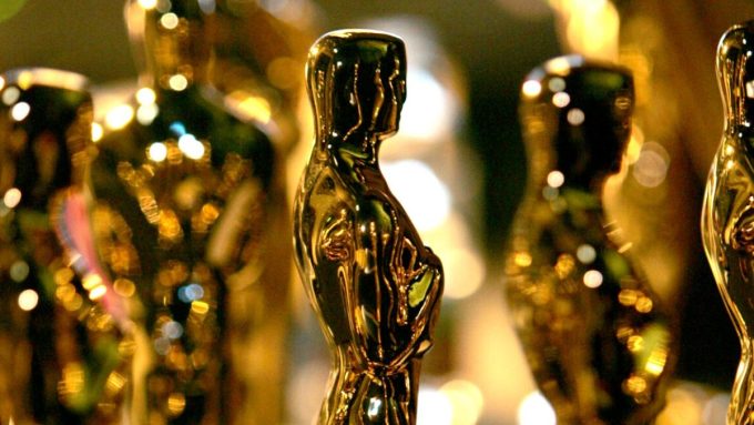 A close-up, shallow-focus shot of several gold Oscar statuettes lined up. The iconic awards gleam under warm stage lighting, with a soft, blurred "bokeh" background creating a prestigious atmosphere for the 98th Academy Awards.