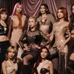 A professional group shot of BINI; several members stand while others are seated, all looking away from the camera with serious expressions. The lighting is dramatic, highlighting their stylish neutral-toned outfits in a studio setting.