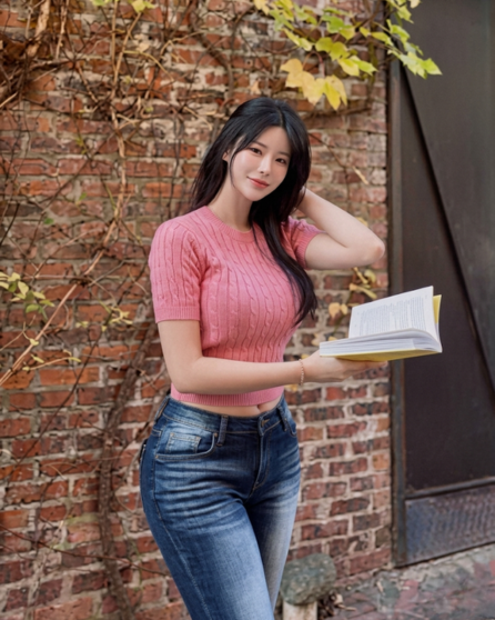 Seoul Bunny holding a book while posing in a pink top and blue jeans.