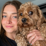 Skylar Mae smiling while holding her brown curly-haired dog.