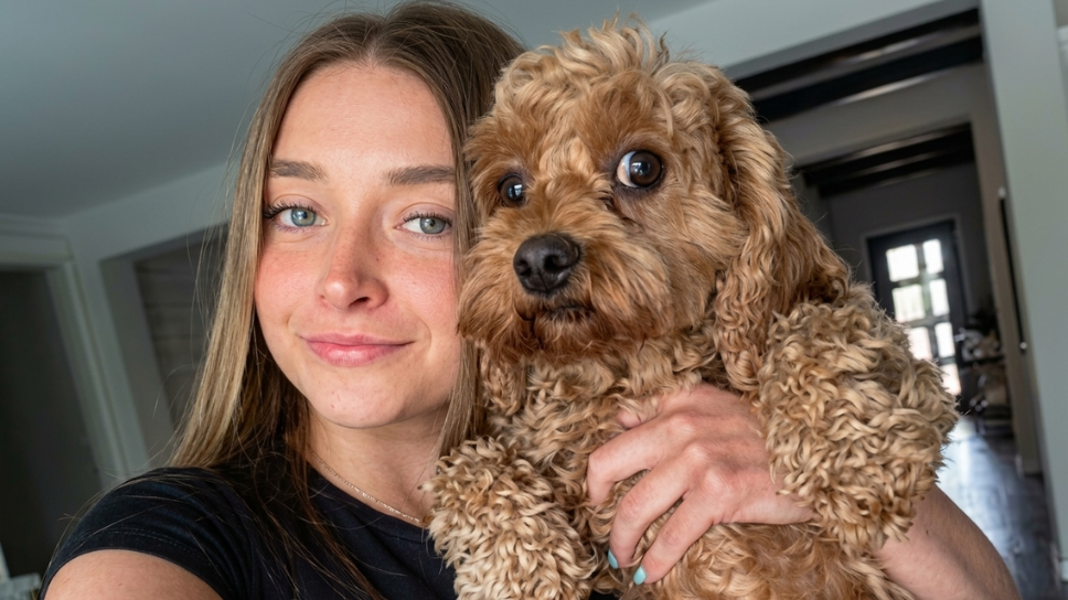 Skylar Mae smiling while holding her brown curly-haired dog.