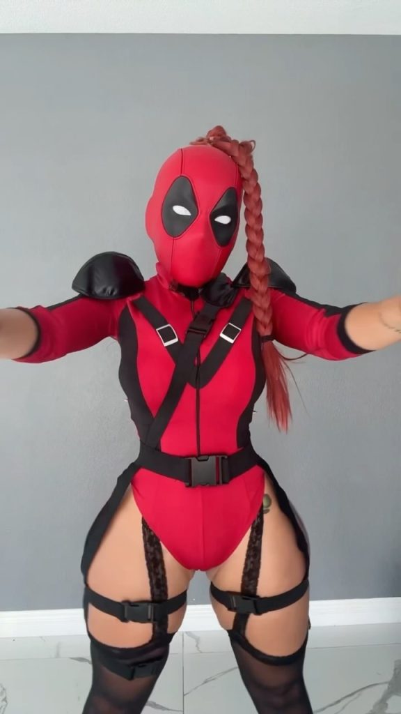 A unique female-inspired Deadpool cosplay featuring a full mask with a long red braided ponytail and a high-waisted red and black tactical suit.
