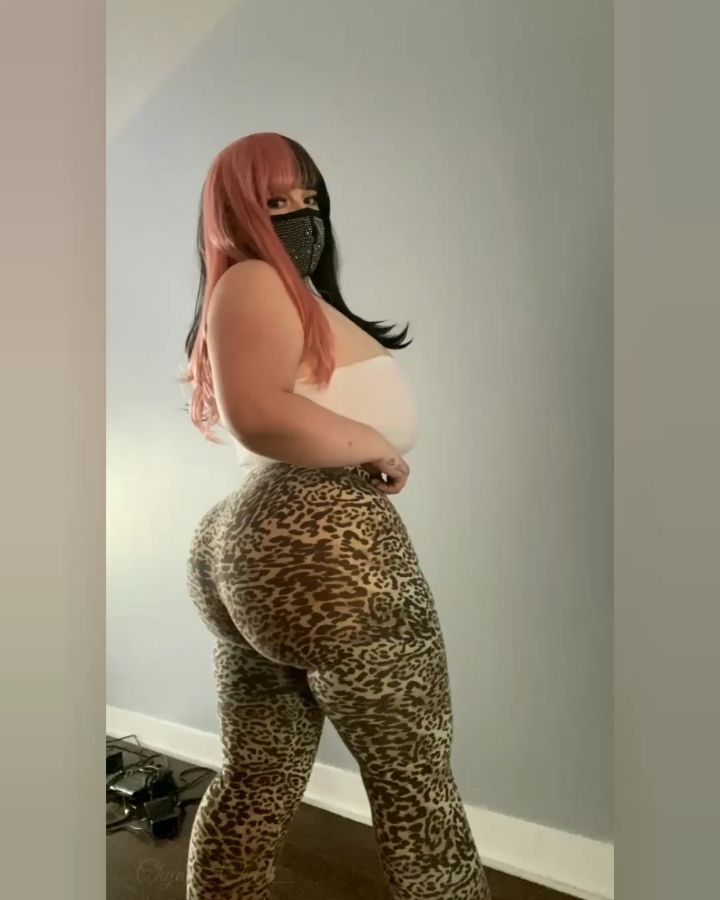 A full-body profile shot of Cosplay Influencers featuring Chyna Chase with half-pink, half-black hair and a studded face mask, wearing a white tube top and high-waisted leopard print leggings.