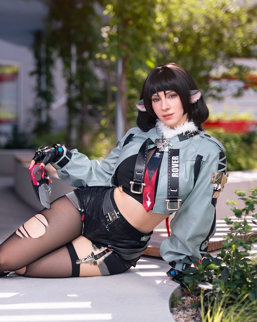 A professional sci-fi photoshoot featuring Enji Night cosplaying Major Motoko Kusanagi from Ghost in the Shell. She poses in a white bodysuit under dramatic pink and blue laser lights, representing the high-quality