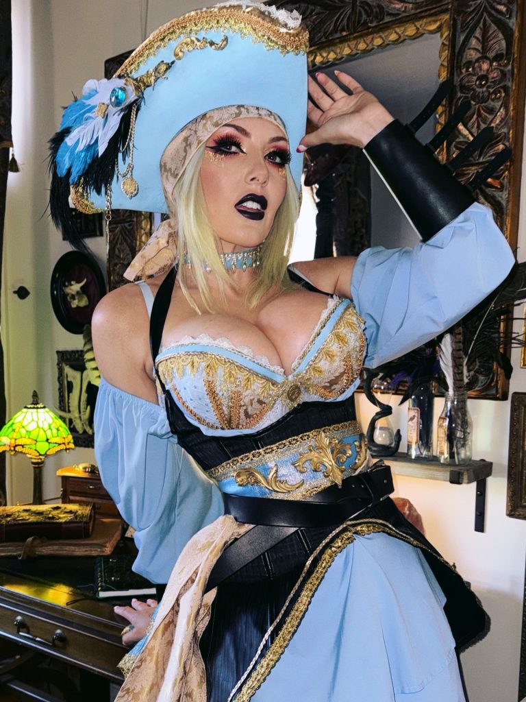 A high-fidelity pirate cosplay featuring a blue and gold corset, a matching tricorn hat with feathers, and dramatic makeup.