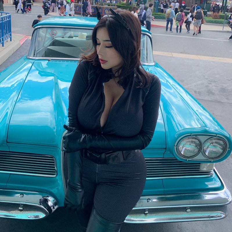 Asian OnlyFans model Maria Nagai posing in a Catwoman cosplay outfit in front of a vintage turquoise car.