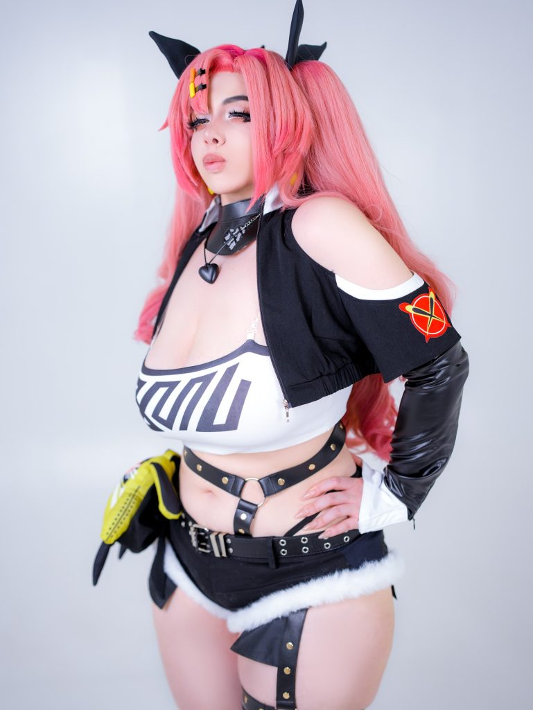 A studio portrait of Cosplay Influencers featuring Mariah Mallad in a detailed pink-haired anime battle suit with black and white accents, featuring a stylized "X" emblem on the shoulder.