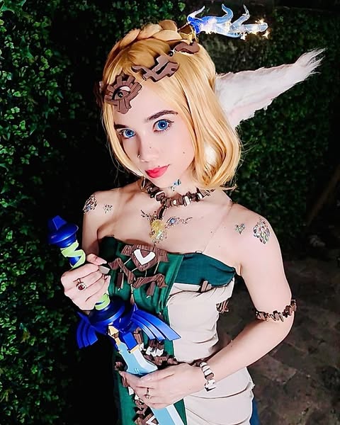 Cosplay Influencers featuring WindyGirk in a Princess Zelda-inspired costume, holding the Master Sword and wearing a green and cream dress with intricate elven jewelry.