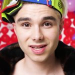 Close-up portrait of influencer Adam Kajumi wearing neon ski goggles and a fur-collared jacket against a background of red and purple balloons, related to investigations into his OnlyFans Management Agency.