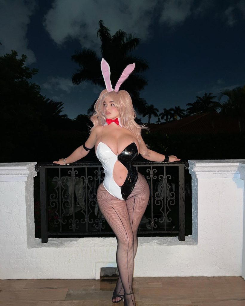 Popular Russian OnlyFans creator wearing a black and white bunny cosplay bodysuit, pink bunny ears, and fishnets on a balcony at night.