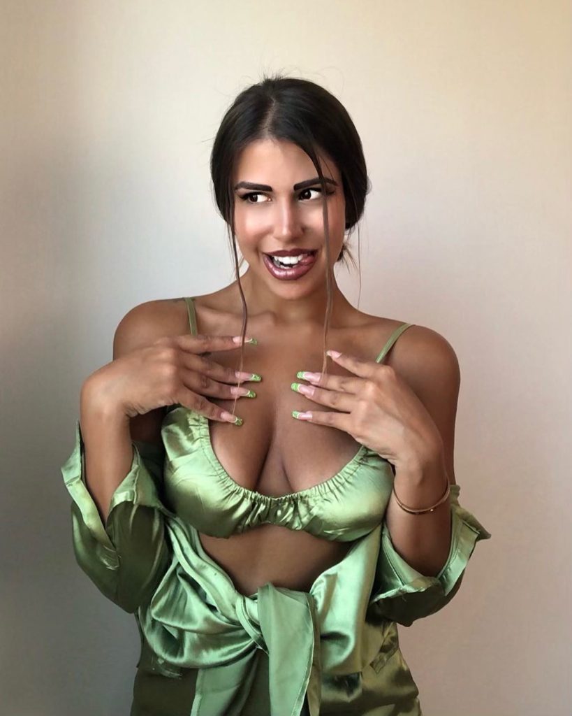 Angelina Piskopani smiling and posing expressively in a green satin bralette and matching outfit.