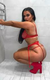 "Irish OnlyFans creator April Rozina crouching in a bathroom wearing a red lace lingerie set and matching red heels.