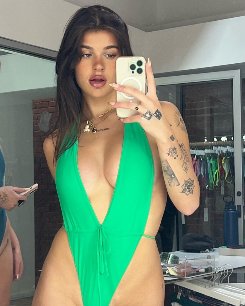 Mirror selfie of Ari Kytsya OnlyFans model wearing a vibrant neon green high-cut swimsuit in a dressing room setting.