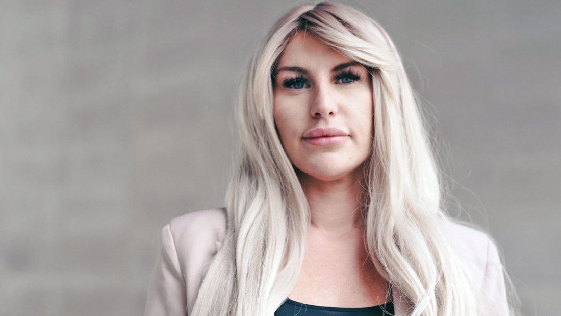 A blonde woman looking directly into the camera during a BBC investigation highlighting exploitative practices where some OnlyFans Managers take up to 70% of creator earnings.