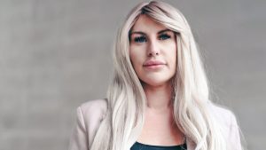 A blonde woman looking directly into the camera during a BBC investigation highlighting exploitative practices where some OnlyFans Managers take up to 70% of creator earnings.