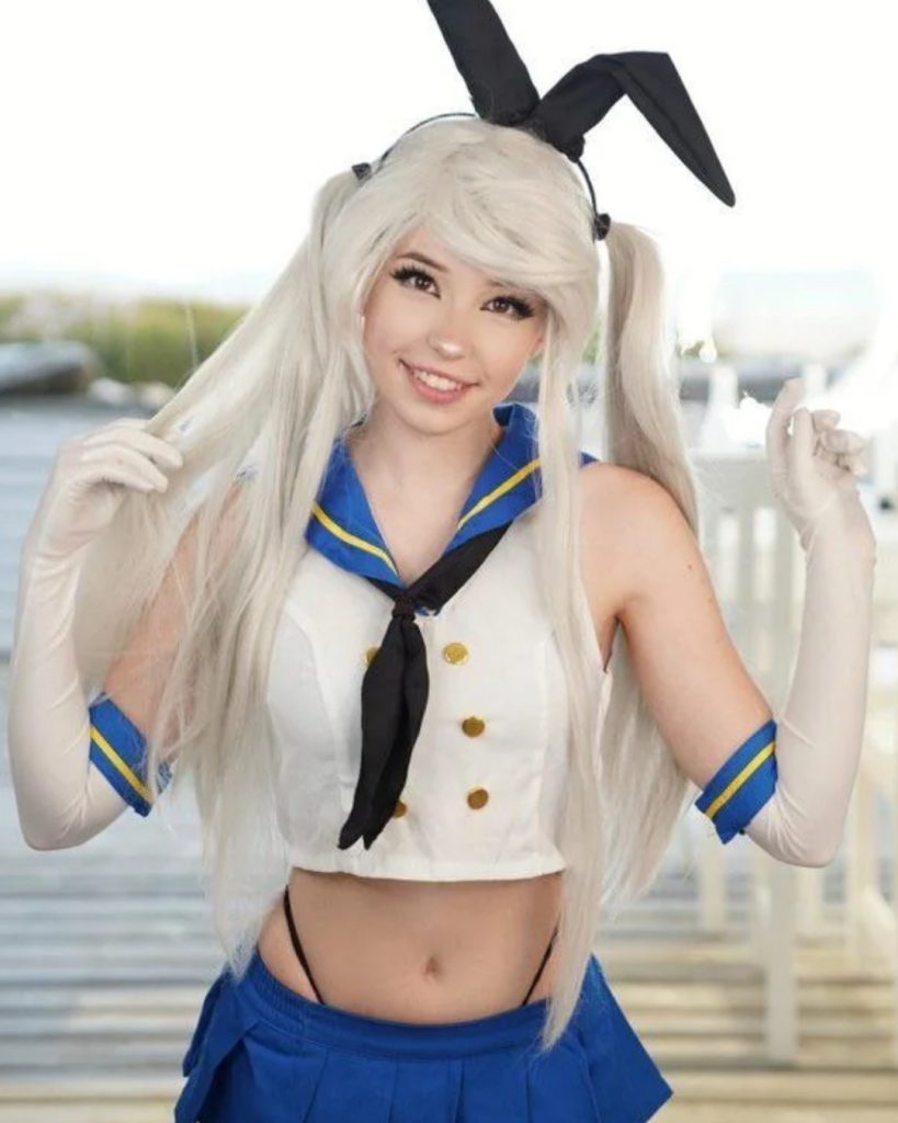 Belle Delphine OnlyFans star posing in a white and blue sailor-style cosplay crop top, blue pleated skirt, long white gloves, and a black bunny ear headband over her platinum blonde hair.