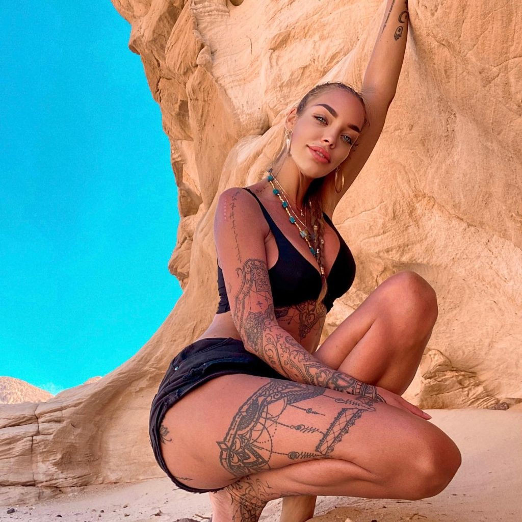 Dorien Rose posing in a black bikini and shorts, crouching in front of a sandstone rock formation.