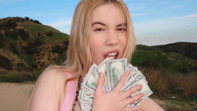 Social media personality Lil Tay flaunting a large fan of one-hundred-dollar bills in front of her face outdoors, highlighting discussions around the Lil Tay OnlyFans launch.