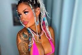 Irish OnlyFans influencer Meghan O'Neill looking to the side, showcasing blonde and pink accented braids, a pink bikini, and a shoulder tattoo.