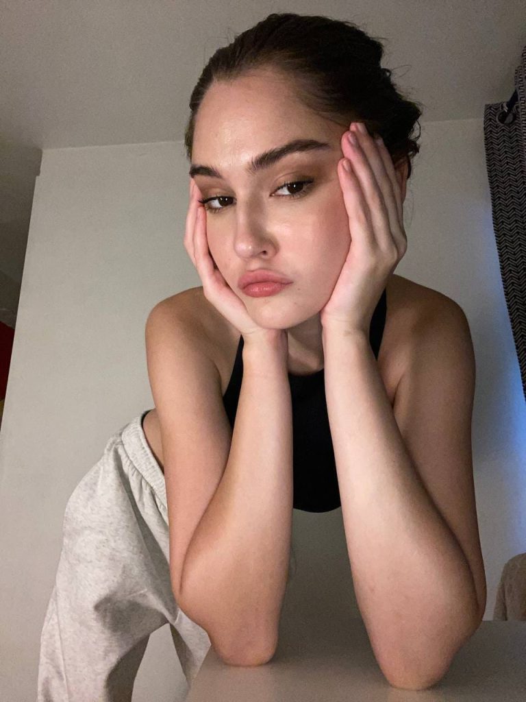A casual indoor selfie of Sonya Blaze, an adult creator on Russian OnlyFans, resting her face in her hands while wearing a black halter crop top and grey sweatpants.