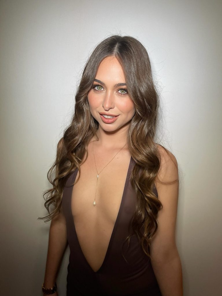 A portrait of Riley Reid with long wavy hair and green eyes, wearing a plunging dark dress and a gold necklace, a classic profile picture for Riley Reid OnlyFans content.