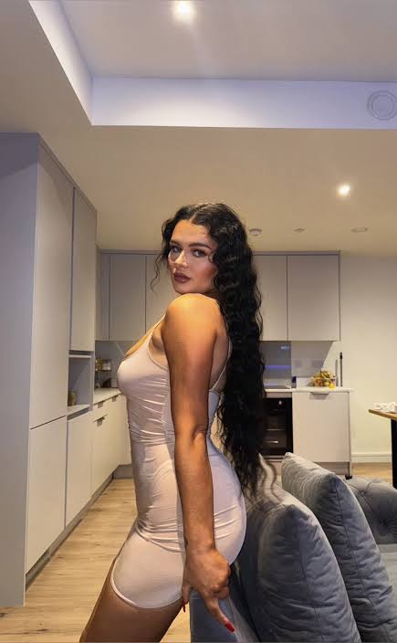 Irish OnlyFans model April Rozina wearing a fitted beige mini dress in a modern kitchen setting