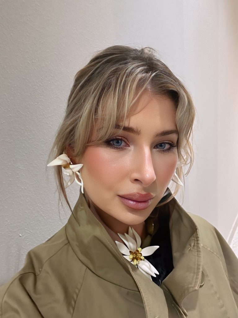Artistic close-up portrait of Amber Brits wearing an olive jacket and intricate white floral earrings and a choker.