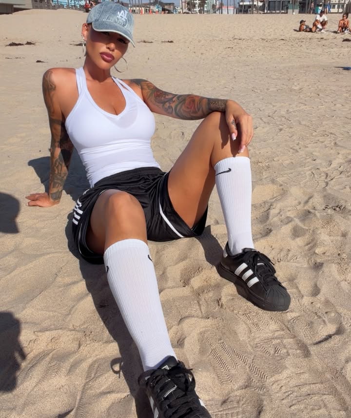 Seated portrait of Amber Rose on the beach wearing a baseball cap and athletic gear, featured as a top Lightskin OnlyFans model.