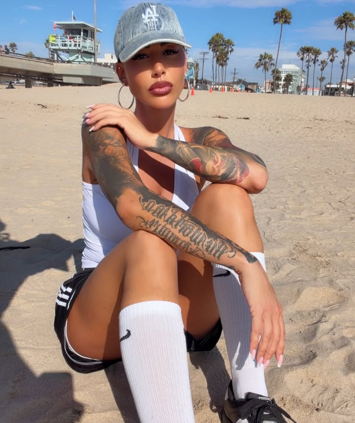Amber Rose relaxing on the beach in a white tank top and cap, listed as a prominent Lightskin OnlyFans creator.