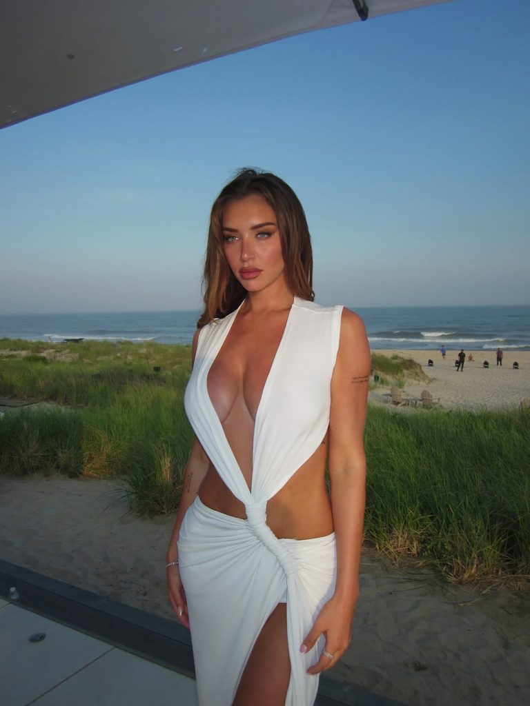 A portrait of Anastasia Karanikolaou OnlyFans star posing in a white cutout dress at a beachside location during the late afternoon.