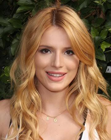 A portrait shot of Bella Thorne with wavy blonde hair, wearing a "BG" initial necklace.