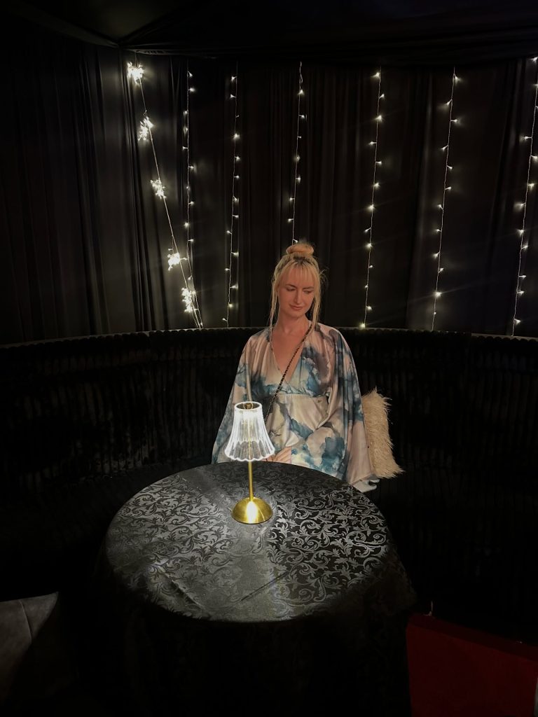 South African OnlyFans model Chevonne Ball sitting at a dimly lit table decorated with fairy lights.