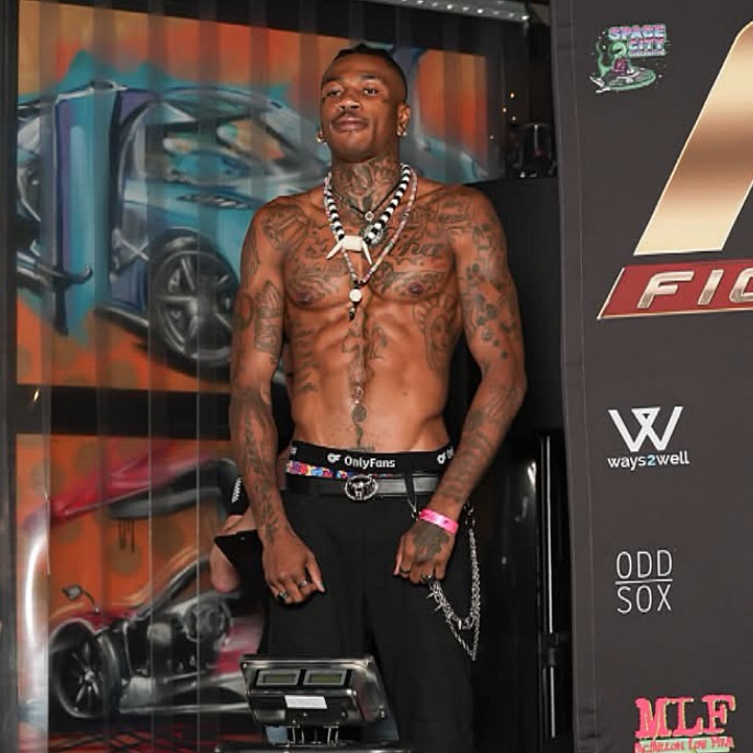 Shirtless Nigerian OnlyFans star Chimereuche-Jackson Nwokeoma posing on stage at a combat sports weigh-in event.