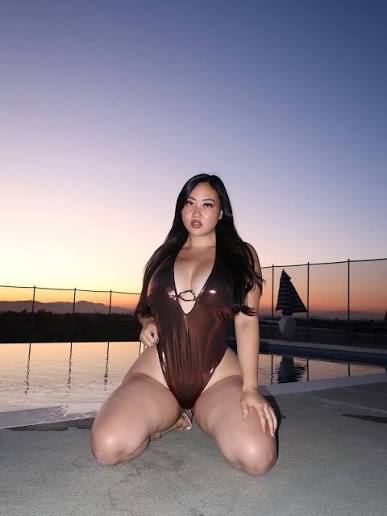 Christie McFit OnlyFans creator posing in a metallic bronze swimsuit by a poolside at sunset.