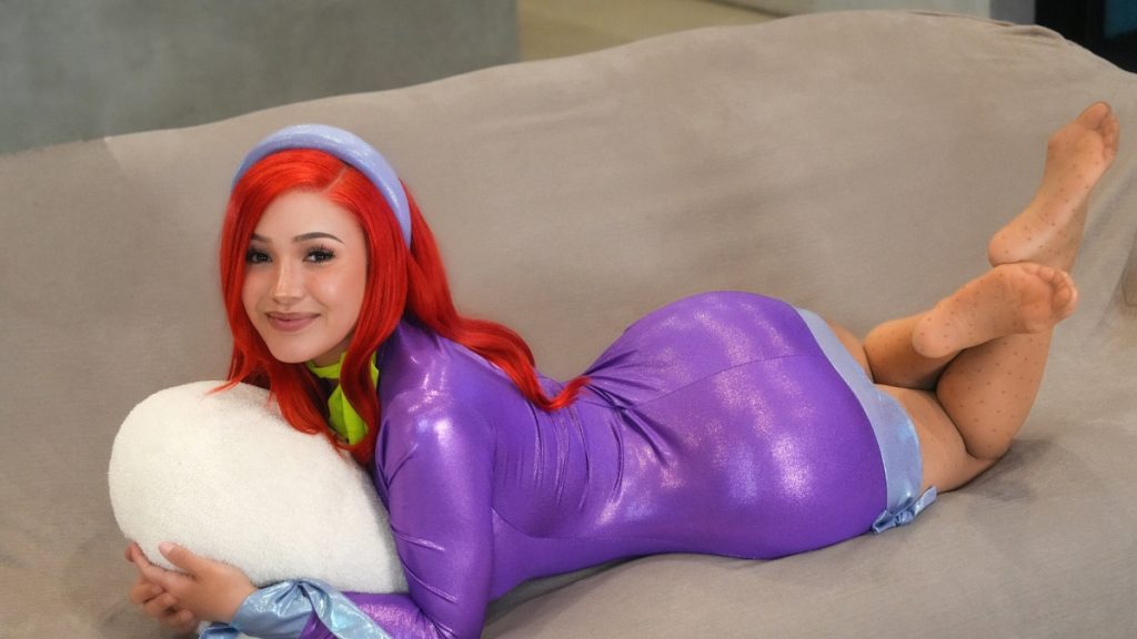Model Cristina in a purple cosplay outfit lying on a couch with arched soles visible, listed among top Best Feet OnlyFans models.