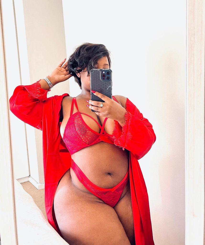 A mirror selfie of Isenako Sihlahla, South African OnlyFans Model, with short dark hair, covering her face with an iPhone while wearing a red lace bra and matching robe.
