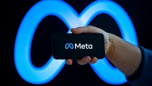 A hand holding a smartphone displaying the Meta logo on its screen against a large, glowing blue neon Meta infinity symbol background. This conceptual image represents discussions surrounding Meta AI adult content copyright policies, training data, and intellectual property issues.