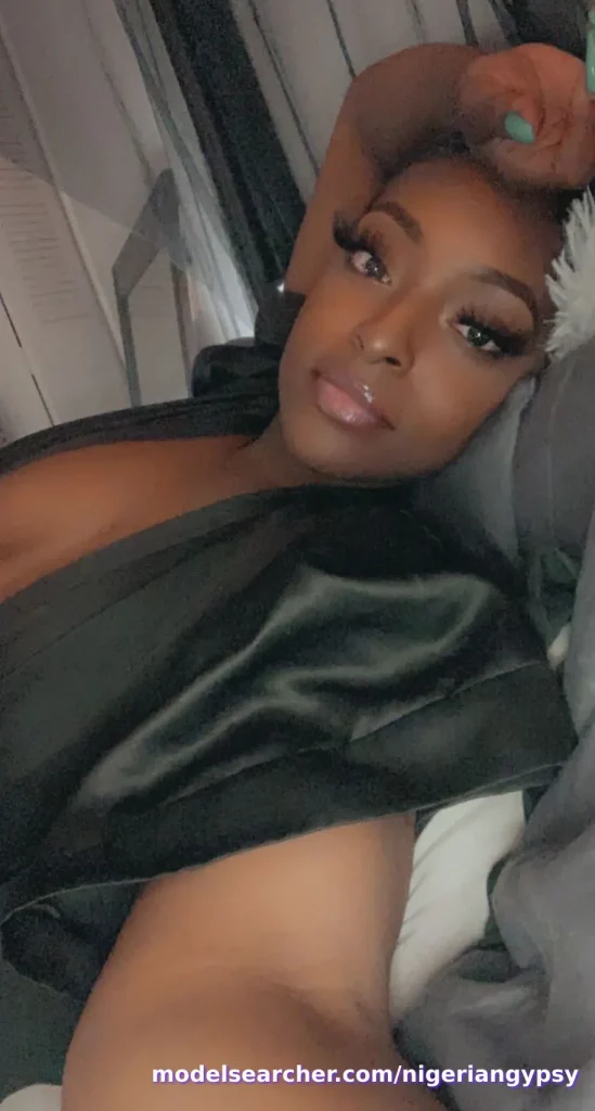 Nigerian OnlyFans creator Nigerian Gypsy taking a close-up selfie while lying down wearing a black satin robe.