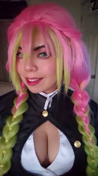 Close-up portrait of Paleseafoam dressed in a Mitsuri Kanroji cosplay, featuring a vibrant pink and green braided wig, green contact lenses, and the signature Demon Slayer uniform with an open chest design.