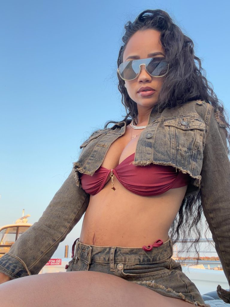 Rosana Joyner, a Cuban OnlyFans model, wearing a cropped denim jacket, burgundy top, and denim shorts while posing outdoors.