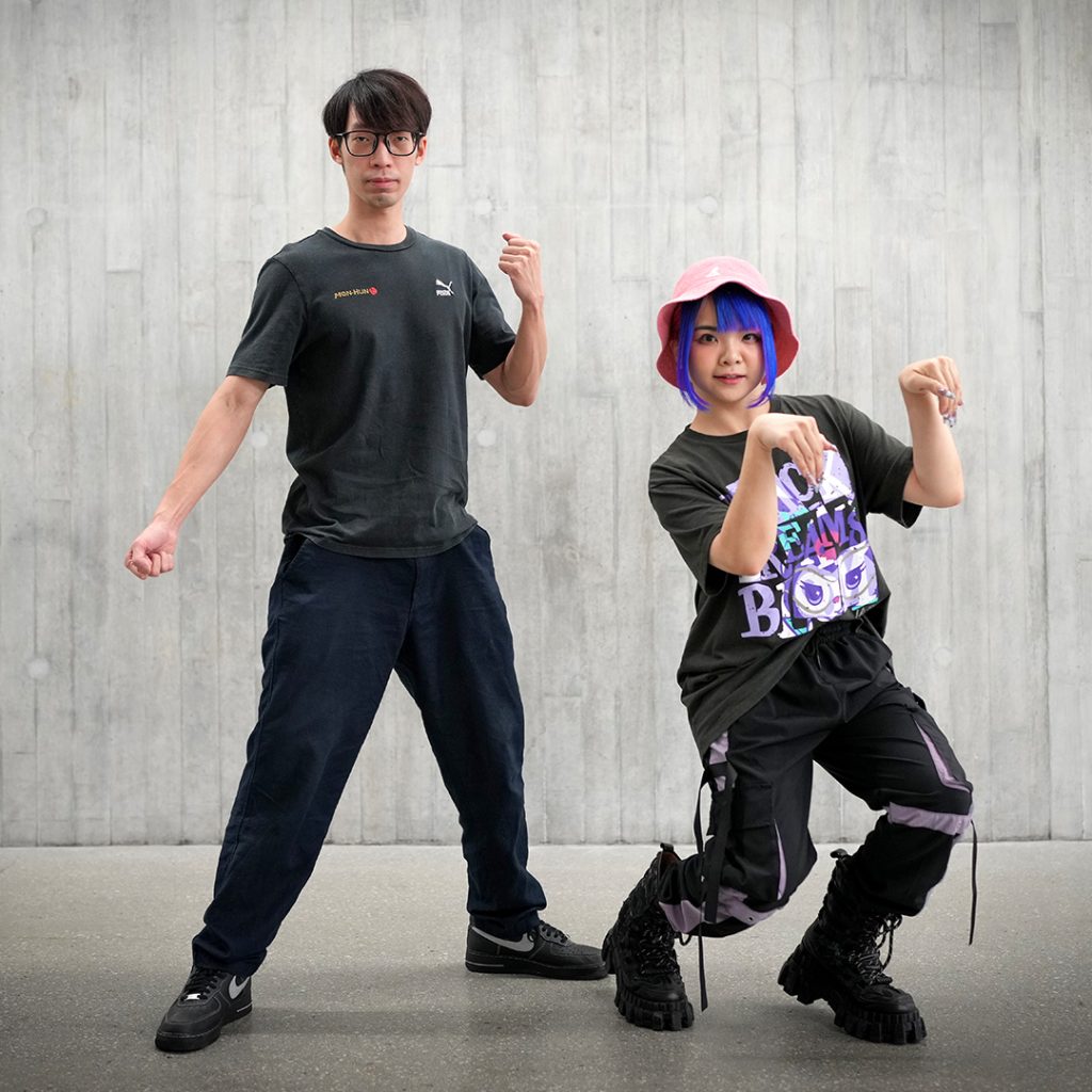 Top Convention Cosplayers featuring a man in a black t-shirt and glasses posing alongside a woman in a pink bucket hat, blue wig, and street style streetwear