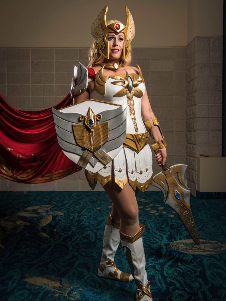 Top Convention Cosplayers featuring She-Ra in full white and gold armor holding a shield, sword, and wearing a winged helmet