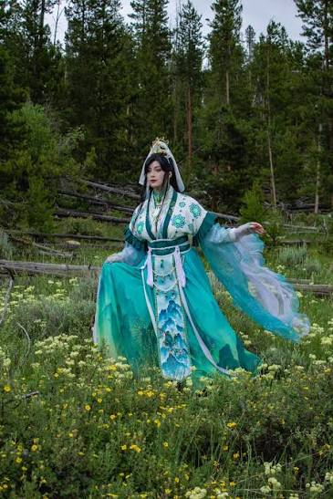Top Convention Cosplayers featuring a woman in a detailed green and white traditional Chinese xianxia-style gown posing in a meadow